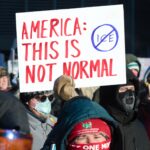 person holding sign that reads "America, this is not normal" with a circle with line through ICE
